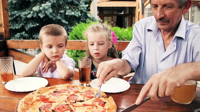 Family eating pizza in front of fireplace. Kids with grandfather for lunch eating tasty pizza at summer cafe. Little children eating unhealthy food outdoors.