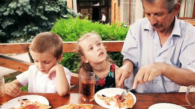 Family having dinner in restaurant. Kids with grandfather for lunch eating tasty pizza at summer cafe. Little children eating unhealthy food outdoors.