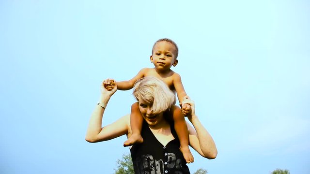 Mom playing with her baby. Happy mother dancing with her baby over blue sky background. Beautiful multiracial family.  Carefree, fun lifestyle.