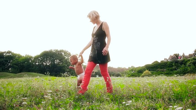 Baby learn to walk. Happy multiracial family, mother and little child is walking a sunny day in the park. Baby taking their first steps.