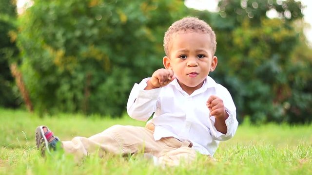 Cute child playing and have fun on the lawn. Funny little afro-american kid is getting to know to the natural world. Cute little kid playing outside. 