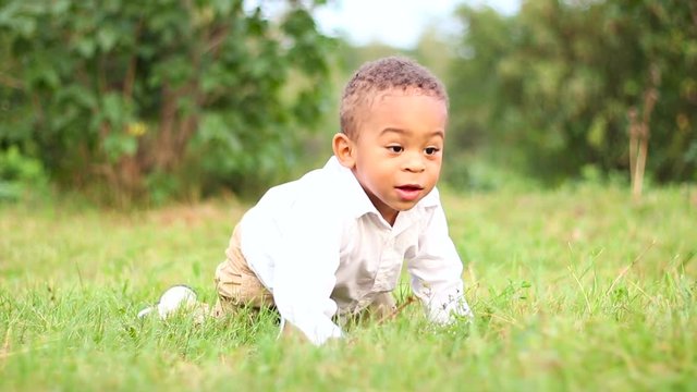 Funny little kid playing outside. Cute little afro-american boy are playing and crawls on grass in the lawn.