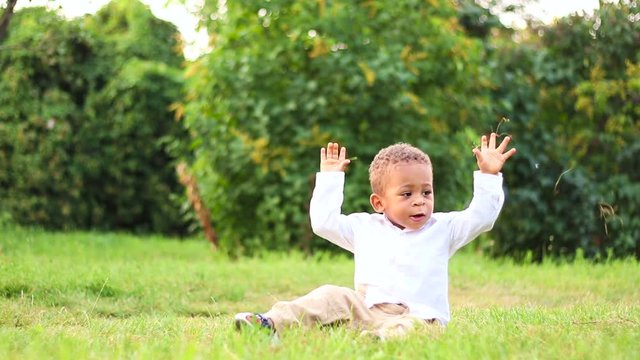 Cute child playing and have fun on the lawn. Funny little afro-american kid is getting to know to the natural world. Cute little kid playing outside. 