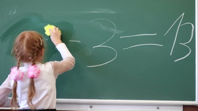 Schoolgirl writes numbers on the blackboard. Mathematics lesson in elementary school. Children at school.