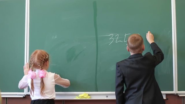Little students writes numbers on the blackboard in class. Mathematics lesson in elementary school.