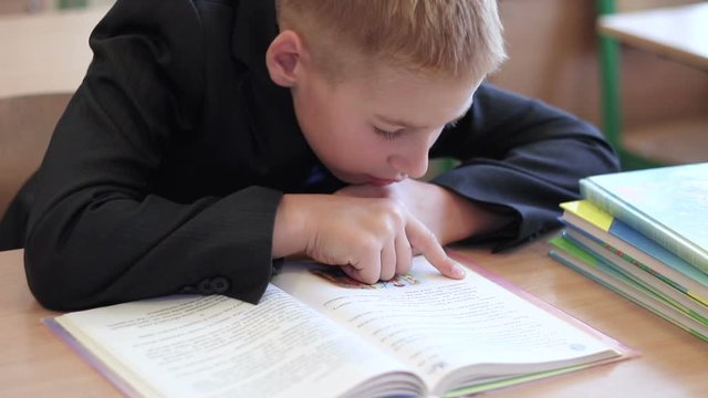 Curious schoolboy sitting in the classroom and reading interesting book. Children at elementary school close-up. Boy doing homework.