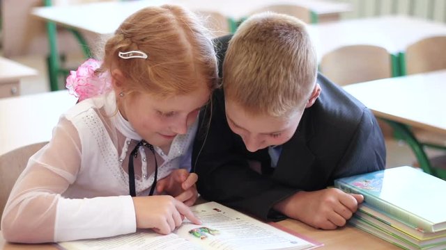 Children on the literature lesson at school. Curious pupils sitting in the classroom and reading interesting book. Children at elementary school close-up.