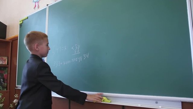 Schoolboy writes numbers on the blackboard. Mathematics lesson in elementary school. Children at school.