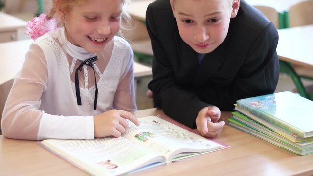 Children on the literature lesson at school. Curious pupils sitting in the classroom and reading interesting book. Children at elementary school close-up.
