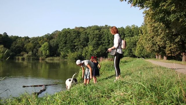 Happy family in the park. Mother with her children and dog walking in summer forest. Mom and kids relaxing by the lake.