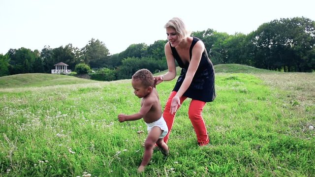 Baby learn to walk. Happy multiracial family, mother and little child is walking a sunny day in the park. Baby taking their first steps. Carefree, fun lifestyle.