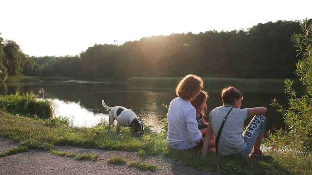 Happy family in the park. Mother with her children and dog walking in summer forest. Mom and kids relaxing by the lake.
