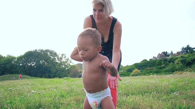 Baby learn to walk. Happy multiracial family, mother and little child is walking a sunny day in the park. Baby taking their first steps. Carefree, fun lifestyle.