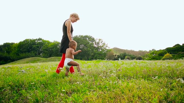 Baby learn to walk. Happy multiracial family. Young mother and her one years old little son for a walk. Mom helping your baby learn to walk.