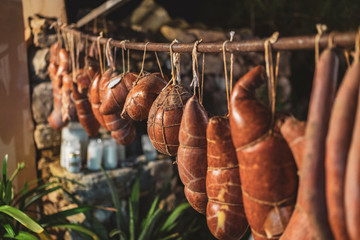 Sobrassadas hanging from a bar with jars of butter in the background