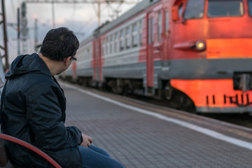 A man sitting on the platform against the background of standing next to the locomotive waiting