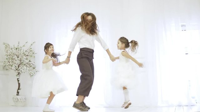 Mom and her daughters hold hands and jump on the stage. They have fun, they dance together. Girls in white elegant dresses, mother in a shirt and trousers. Preparing for the school ball