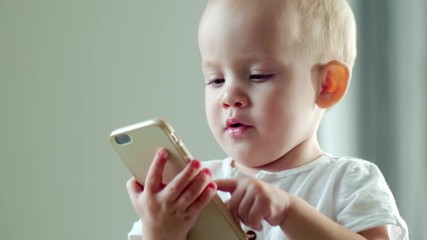Adorable baby boy tapping on touchscreen of modern smartphone while learning new gadget