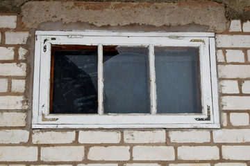 Fototapeta na wymiar Old dirty white wooden window with broken glass pane on brick wall outdoors.
