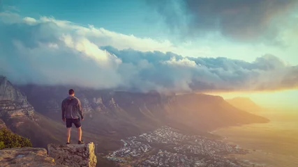 Photo sur Plexiglas Montagne de la Table Young man standing on the edge at the top of Lion's head mountain in Cape Town with a beautiful sunset view
