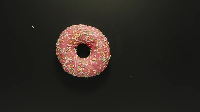 TOP VIEW: Pink donut falls on black surface of table - Slow Motion