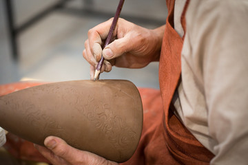 Ceramic workshop, the master puts otnament on unfired earthenware jug. Close-up of master hands. Made by hand, a hobby. Background illustrating the manual work with clay.