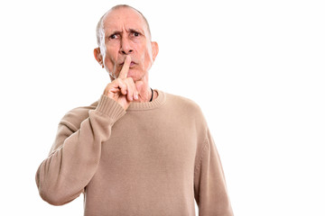 Studio shot of angry senior man with finger on lips