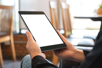 Mockup image of a woman holding black tablet pc with blank white screen while sitting in cafe