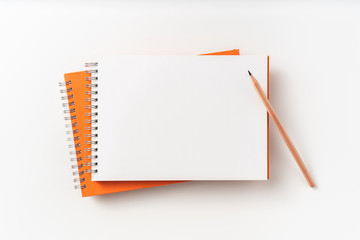 Top view of orange spiral notebook, page, pencil