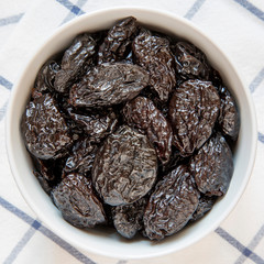 Dry prunes in a bowl, overhead view. Flat lay, from above, top view.