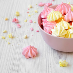 Mini meringues in a pink bowl over white wooden surface, side view. Closeup.