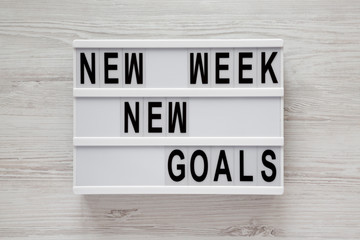 Modern board with text 'New week new goals' over white wooden surface, top view. From above, flat lay, overhead.