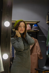 girl in a gray elegant dress and a green beret looks in the mirror and smiles