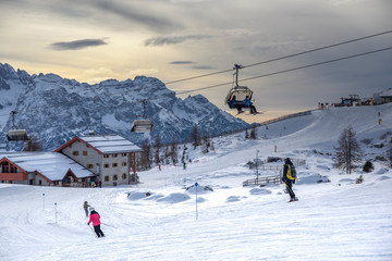 Fototapeta na wymiar ski slopes with skiers and chairlift at sunset. Trentino, Italy