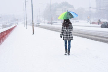 Back view on women walking in the city on blizzard. Woman walks through snow on sidewalk