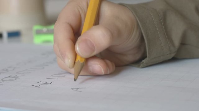 Child writing alphabet letters ABCDE with a pencil on a squared notebook extreme close up