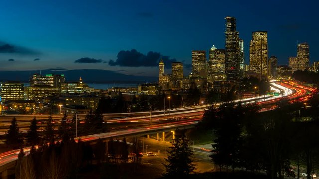 Time lapse of long exposure auto traffic light trails on interstate freeway I5 and moving clouds over downtown city skyline in Seattle Washington from daylight sunset into blue hour at night 4k ultra 