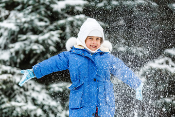 A little girl in a white suit in the winter woods throws snow