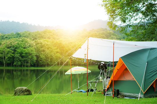 nature orange with green camping tent and tarp with tent accessory on meadow with lake or river and tree mountain in forest for holiday trekking relax on winter or summer and sunlight at ched khot
