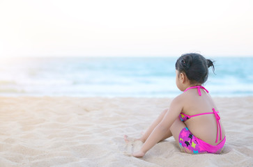 Fototapeta na wymiar Asian child cute or kid girl sit on beach or blue sea and playing white sand alone for travel on summer holiday relax with happy fun and wear bikini on warm sunlight with space