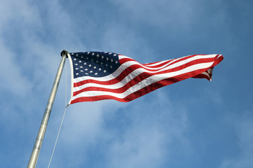 Naklejka premium American flag on a pole flying against bright blue skies