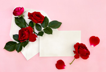 Beautiful flowers red roses in postal envelope and blank sheet with space for text and red petal roses on a pink paper background. Top view, flat lay