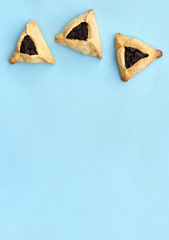 Triangular cookies with poppy seeds ( hamantasch or aman ears ) for jewish holiday of purim celebration on blue paper background with space for text. Top view, flat lay