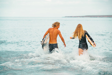 Surfers at the beach- Smiling couple of surfers walking on the beach and having fun in summer. Extreme sport and vacation concept