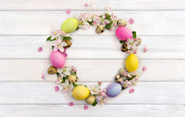 Easter decoration. Circle Easter frame of pink flowers apple tree, colored easter eggs and quail eggs on background of white painted wooden planks with space for text. Top view, flat lay