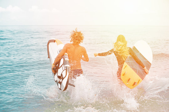Surfers at the beach- Smiling couple of surfers walking on the beach and having fun in summer. Extreme sport and vacation concept