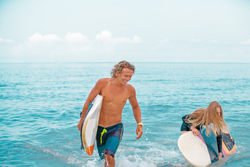 Surfers at the beach- Smiling couple of surfers walking on the beach and having fun in summer. Extreme sport and vacation concept