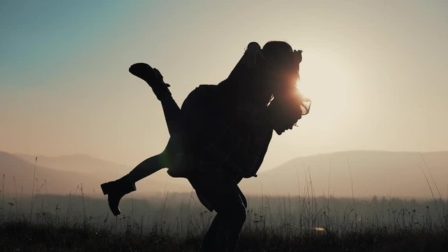 Young couple in love on vacations enjoying mountains. Attractive man is carrying girlfriend on his shoulders and whirls her. Having fun