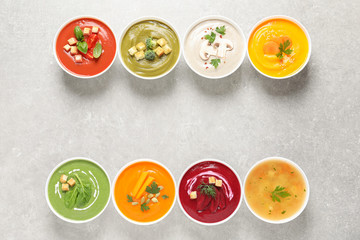 Various cream soups in bowls and space for text on grey background, top view