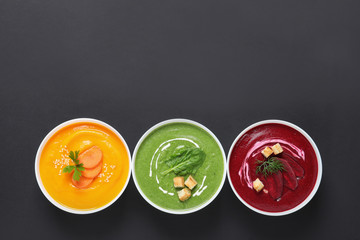 Various cream soups in bowls and space for text on black background, top view
